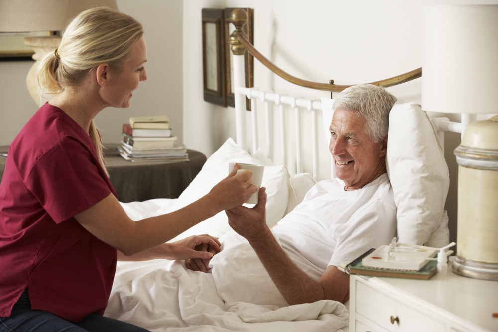 Health Visitor giving senior male hot drink in Bed