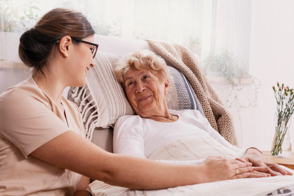 Critical care nurse holding hands with elderly woman in bed, providing high-level private duty nursing care at home.