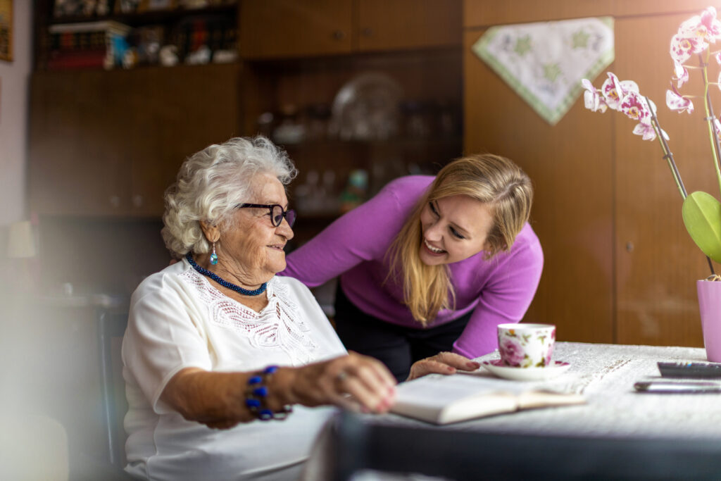 Private duty nurse smiling and supporting elderly woman at home, representing personalized in-home nursing care.