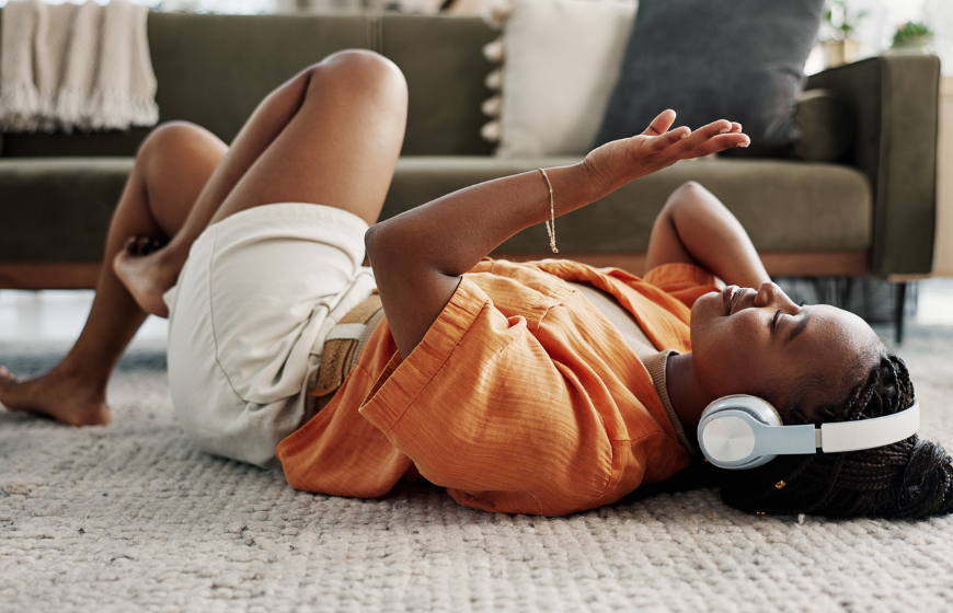 Black woman relaxing on the floor and listening to music through her headphones