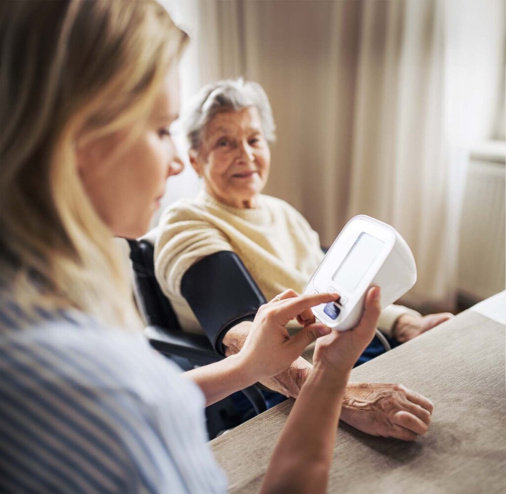 Photo of a woman taking blood pressure of another smiling woman.