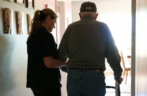 An Alliance Homecare Agency caregiver assisting an elderly man with a walker in a home setting, demonstrating professional home care services and mobility support.
